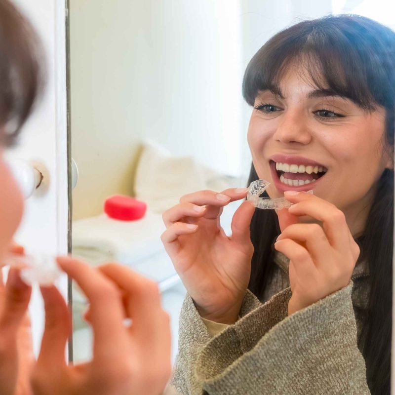 Women in mirror holding clear aligners.