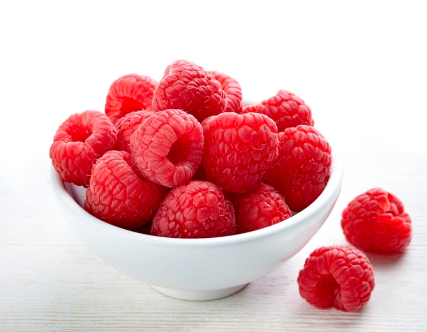 White bowl with raspberries on white surface