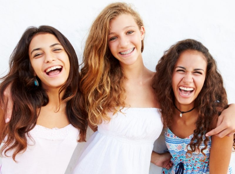 Three smiling teenage girls leaning against wall