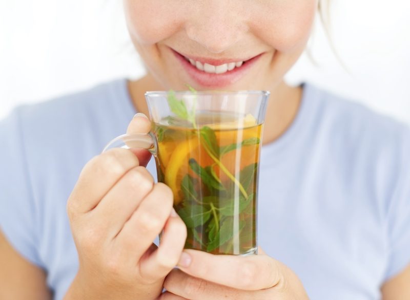 Close-up of woman smiling and holding up a cup of herbal tea